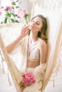 Cute tender young girl with blond hair in white clothes and lace underwear surrounded by pink peonies on the bed Royalty Free Stock Photo