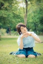 Cute Thai schoolgirl is sitting on the grass and doing heart symbol in childish color. Royalty Free Stock Photo