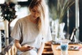 A cute thin blonde girl,dressed in casual style,drinks coffee and looks at her phone in a coffee shop.