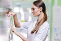 A cute thin lady with dark hair and glasses,wearing a lab coat,takes something from the shelf in an up-to-date pharmacy.