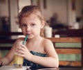 Cute thinking kid girl drinking juice in cafe with serious look