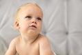 Cute thoughtful baby boy sitting on the bed against the grey background. Copy space Royalty Free Stock Photo