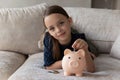 Cute thrifty little girl put coin into piggy bank