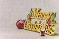 Cute tiny figurine of Santa Claus on a glitter silver snow background with the golden words Merry Christmas and a Christmas Tree Royalty Free Stock Photo