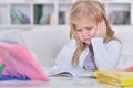 Cute tired schoolgirl sitting at the table and doing homework Royalty Free Stock Photo