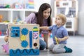 Cute toddler baby and mom playing with busy board at home or daycare. Children`s educational toys. Wooden game diy board Royalty Free Stock Photo