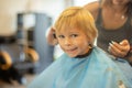 Cute toddler blond boy, having haircut in hairdresser salloon