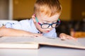 Cute toddler boy with down syndrome with big glasses reading intesting book Royalty Free Stock Photo