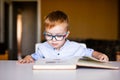 Cute toddler boy with down syndrome with big glasses reading intesting book Royalty Free Stock Photo