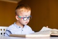 Cute toddler boy with down syndrome with big glasses reading intesting book