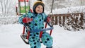 Cute toddler boy enjoying a swing ride in a snowy winter park. Concept of outdoor fun and joy, kids playing in snowfall Royalty Free Stock Photo