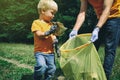 Cute toddler boy and his father collecting garbage in the park. Volunteers family picking up litter in the forest. Environmental