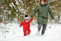 Cute toddler boy and his grandma having fun on a walk in snow covered pine forest on chilly winter day