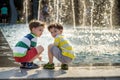 Cute toddler boy and older brothers, playing on a jet fountains with water splashing around, summertime Royalty Free Stock Photo