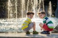Cute toddler boy and older brothers, playing on a jet fountains with water splashing around, summertime Royalty Free Stock Photo