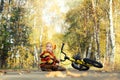 Cute toddler boy sitting on empty road in autumn park looking on falling orange leaves. Child`s bicycle lies nearby. Fall vibes Royalty Free Stock Photo