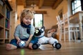 A cute toddler boy sitting indoors at home, playing with robotic dog. Royalty Free Stock Photo