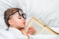 A cute toddler boy is sleeping in a round glasses with an old book under a white blanket. Royalty Free Stock Photo