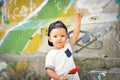 Cute toddler boy in street style clothes and a cap with a big watermelon candy on a graffiti background.