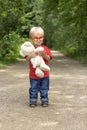 Cute toddler boy with toy glasses and plush bear standing on rural road. Little baby outdoor