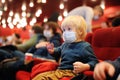 Cute toddler boy wearing face mask watching cartoon movie in the cinema after quarantine. Lifting virus lockdown. Social Royalty Free Stock Photo