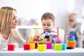 Cute toddler baby playing with wooden hammer block toy. Woman mother or teacher teaching kid in nursery Royalty Free Stock Photo