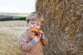 Cute toddler eating German pretzel on goden hay field