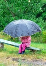 Cute toddler girl with big umbrella sitting in the garden by rainy day Royalty Free Stock Photo