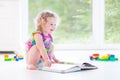 Cute toddler girl with blond curly hair reading book Royalty Free Stock Photo