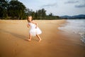 Cute toddler girl with blonde hair in a white tutu dress running on a sandy beach at sunset. Happy childhood memories Royalty Free Stock Photo