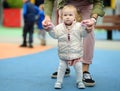 Cute toddler girl having fun on outdoor playground. Young father is teaching his little daughter to walk. First step of baby. Royalty Free Stock Photo