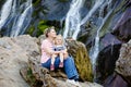 Cute toddler girl and mother sitting near water cascade of Powerscourt Waterfall, the highest waterfall in Ireland in co