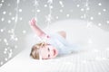 Cute toddler girl playing on a bed between Christmas lights Royalty Free Stock Photo