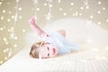 Cute toddler girl playing on a bed between warm soft Christmas l