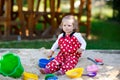 Cute toddler girl playing in sand on outdoor playground. Beautiful baby in red gum trousers having fun on sunny warm Royalty Free Stock Photo