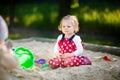 Cute toddler girl playing in sand on outdoor playground. Beautiful baby in red gum trousers having fun on sunny warm Royalty Free Stock Photo