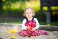 Cute toddler girl playing in sand on outdoor playground. Beautiful baby in red gum trousers having fun on sunny warm Royalty Free Stock Photo