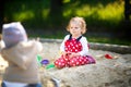 Cute toddler girl playing in sand on outdoor playground. Beautiful baby in red gum trousers having fun on sunny warm Royalty Free Stock Photo