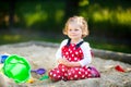 Cute toddler girl playing in sand on outdoor playground. Beautiful baby in red gum trousers having fun on sunny warm Royalty Free Stock Photo