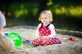 Cute toddler girl playing in sand on outdoor playground. Beautiful baby in red gum trousers having fun on sunny warm Royalty Free Stock Photo