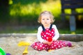 Cute toddler girl playing in sand on outdoor playground. Beautiful baby in red gum trousers having fun on sunny warm Royalty Free Stock Photo