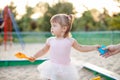 Cute toddler girl playing in sand on outdoor playground.