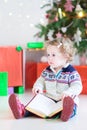 Cute toddler girl reading a book under a Christmas tree Royalty Free Stock Photo