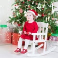 Cute toddler girl in red dress and santa hat near Christmas tree Royalty Free Stock Photo