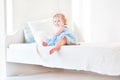Cute toddler girl sitting on a white bed at home