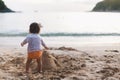 Cute toddler girl standing alone on the beach at sunset Child build sandcastle and looking on the waves, silhouette of Royalty Free Stock Photo