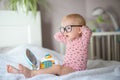 Cute toddler in glasses sitting on bed with a toy laptop. Royalty Free Stock Photo