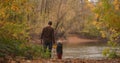 Cute toddler is holding hand of his father in forest, man and child are standing together on calm shore of lake at