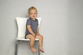 Cute toddler sitting on the chair against gray wall and looking at camera. Copy spase