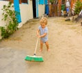 A cute toddler sweeping a yard in the caribbean